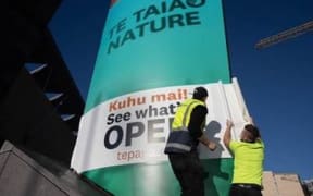 Two workers paste a sign that informs the public Te Papa is open to signage in front of the museum.