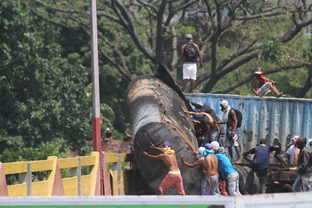 Demonstrators trying to get the trailer of a tanker that is blocking the Simon Bolivar bridge on the border between Colombia and Venezuela off the bridge.