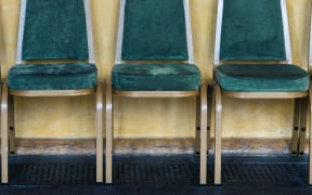 Green chairs lined up against a yellow wall in a waiting area