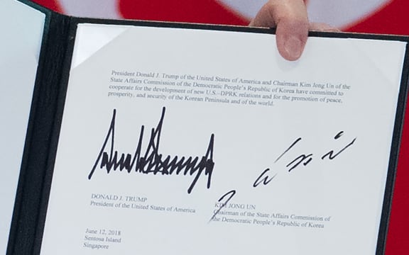 The signatures of US President Donald Trump (L) and North Korea's leader Kim Jong Un (R) are seen on a document held up by Trump following a signing ceremony during their historic US-North Korea summit