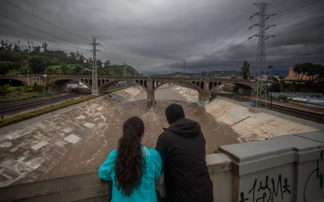 A couple watches the high water level of the Los Angeles river after heavy rains on December 24, 2025 in Los Angeles, California.