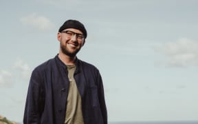 Jeremy Redmore smiles casually in front of a grey background