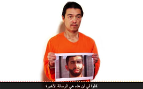 An image obtained from a video uploaded on YouTube on January 27, 2015, of Japanese hostage Kenji Goto  holding a photograph allegedly showing fellow hostage Jordanian pilot Maaz al-Kassasbeh.