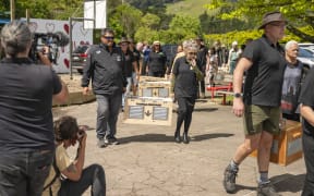 A procession of people carrying wooden boxes that contain kiwi ready to be released. It takes two people on either side of the box to carry it.