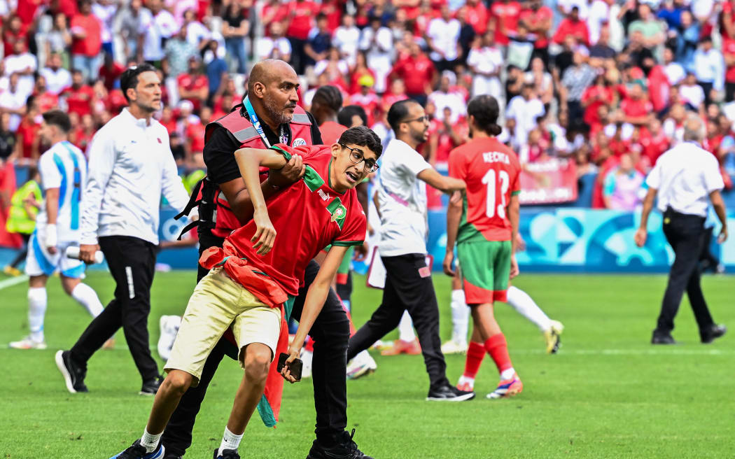 A member of security holds a fan after numerous Morocco's fans invaded the pitch at the end of the men's group B football match against Argentina during the Paris 2024 Olympic Games in Saint-Etienne.