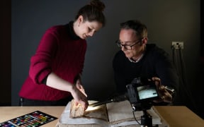 Conservator Sally Kilby and Błażej Mikuła photograph inside the folds of a medieval manuscript that was used as the cover for another book later on.