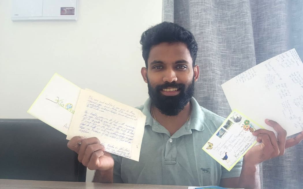 Photo of a man holding up a few letters and postcards, with more letters spread out on the table in front of him.