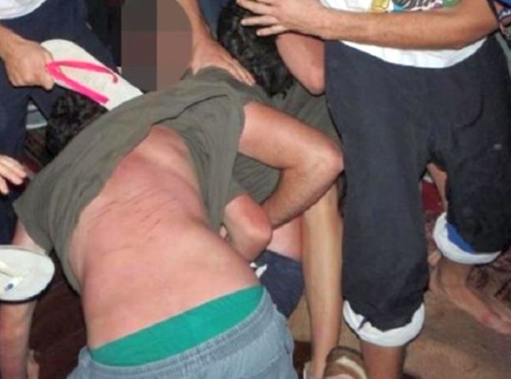 A student is beaten with ribber jandals during a hazing ritual.