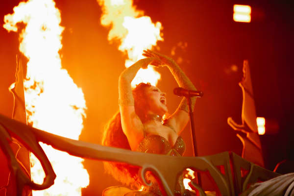 Chappell Roan raises her hands and opens her mouth wide while performing with digital flames behind her.