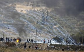Palestinian protesters run for cover amidst smoke during clashes with Israeli security forces, as protests continue in the region over US President Donald Trump's recognition of Jerusalem as its capital.