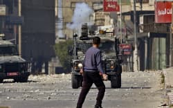 A Palestinian youth holds a rock as he faces an Israeli military vehicle, during a raid on the occupied-West Bank city of Nablus, on 22 February 2023.