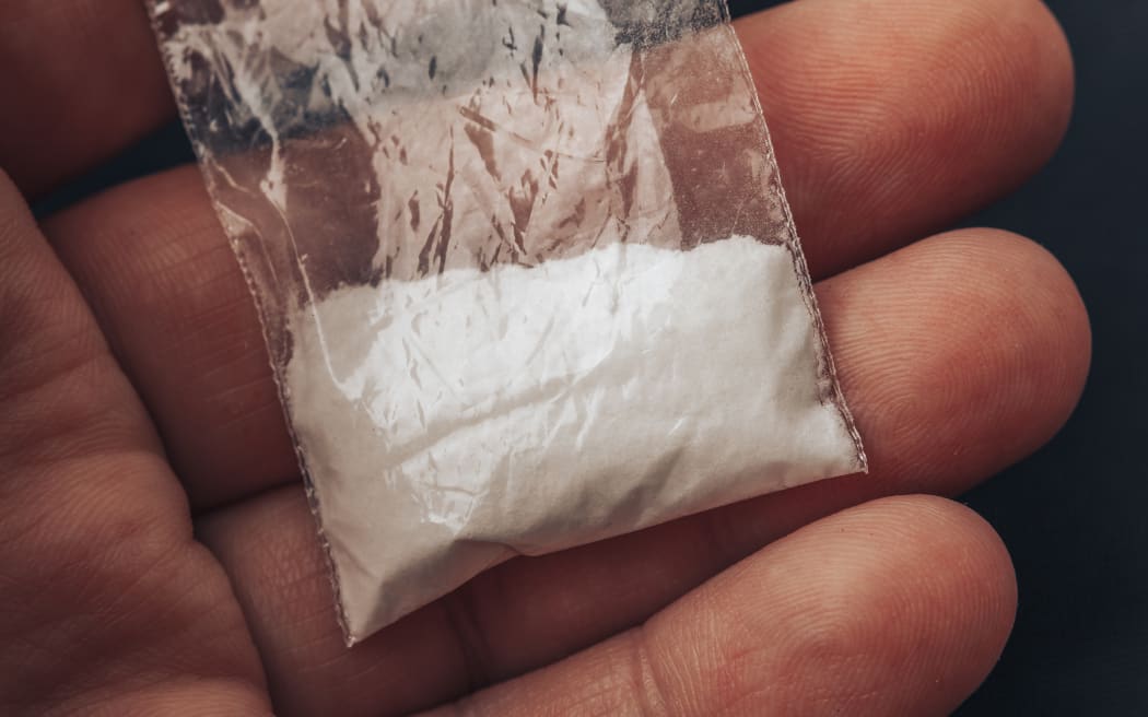 Plastic packet with cocaine powder or another drugs in mans hand. Close-up macro photo.