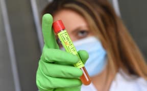 Themed picture, symbolic photo: Corona vaccine. Woman with mask holds a corona test, with high pressure research is underway worldwide on the development of a vaccine versus the corona virus.