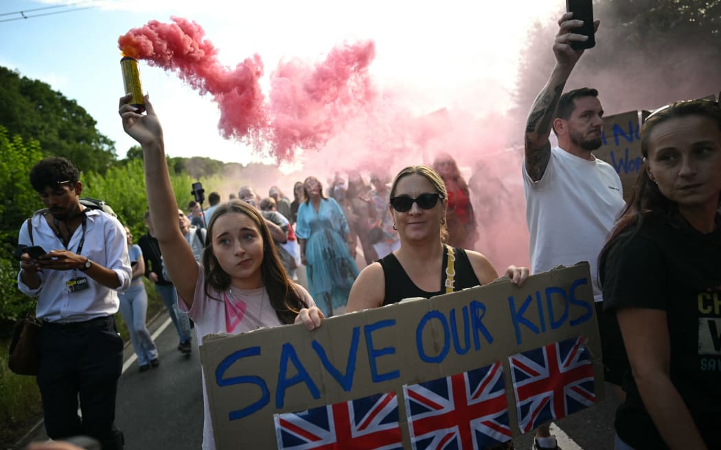 Protesters march with a flare and placards away from The Bell Hotel, believed to be housing asylum seekers, in Epping, northeast of London on July 20, 2025 after police charged an asylum-seeker with sexual offences  earlier this month.  (Photo by JUSTIN TALLIS / AFP)