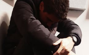 A staged photo of a young man hunched over, used to illustrate the use of seclusion rooms or mental health issues.