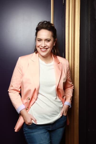 Actress and comedian Kura Forrester stands smiling with hands in pocket.