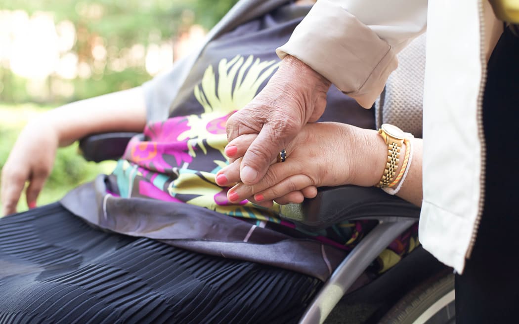 Old people , husband holding his wife is hands while  she in a wheel chair