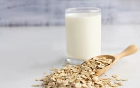 A glass of milk and oats in spoon.
