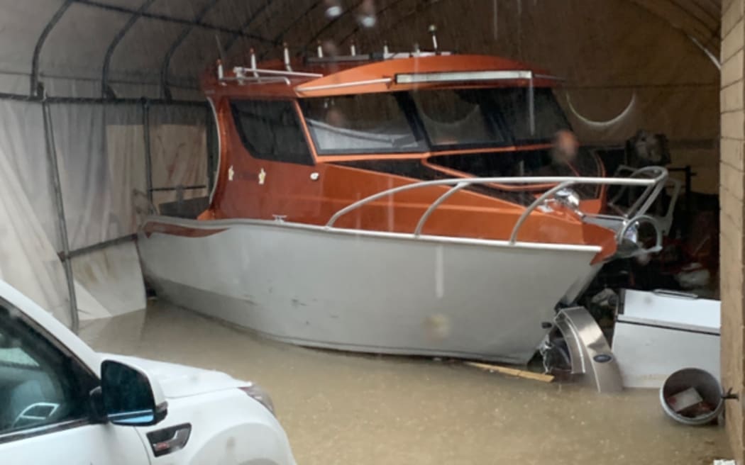 A boat and car are partially submerged in flood waters at a Blockhouse Bay home during Auckland's wild weather at Easter, April 2025.