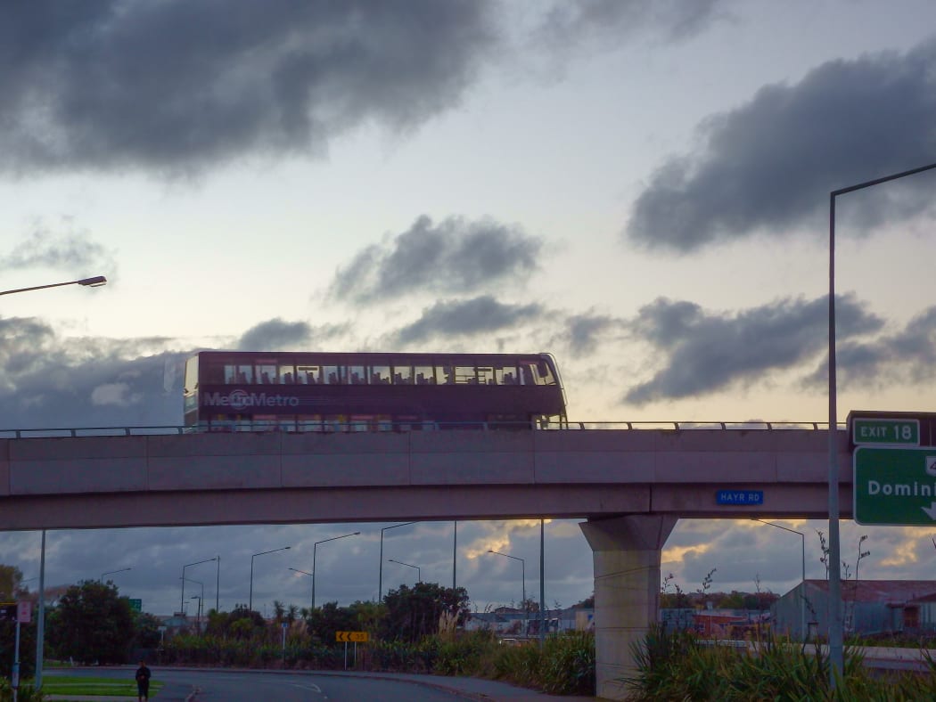 Double decker bus goes on a flyover against a back lit sky in Auckland New Zealand.