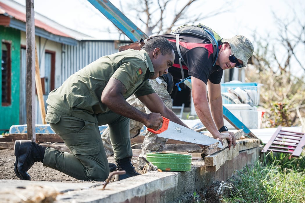 A member of the New Zealand Army helps a local repair damage on a home.