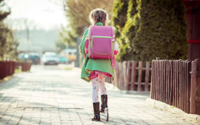 girl goes to school on a scooter. back view