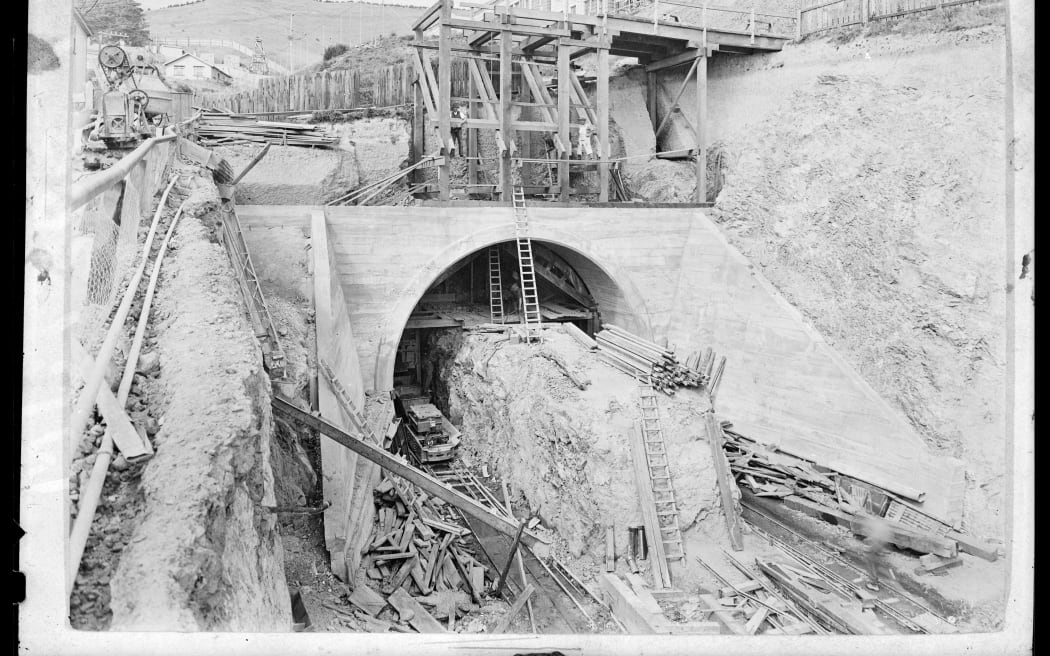 Archival image from circa 1931 of tunnel construction showing concrete entrance, scaffolding and wood and section of un-dugout rock in tunnel entrance being used to work off