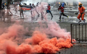 Protesters hurl stones to Kenya police officers amid clouds of teargas during clashes in downtown Nairobi on June 25, 2025 during a planned day of protest marking the first anniversary of the storming of the parliament. Marches in Kenya to mark a year since massive anti-government demos turned violent on Wednesday, with two killed and running battles between protesters and police, who flooded Nairobi's streets with tear gas and sealed off government buildings with barbed wire. (Photo by Luis TATO / AFP)