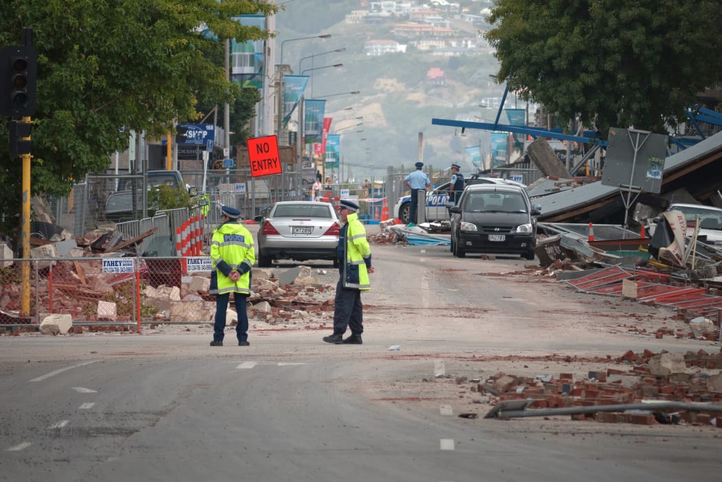 Police stand by amid fallen debris in a cordoned-off street in Christchurch on February 23, 2011 a day after the deadly earthquake.