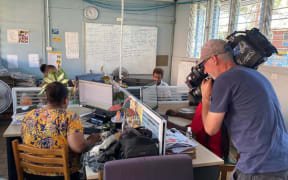 A cameraman from Australia films in the SIBC newsroom while reporters get on with their work.