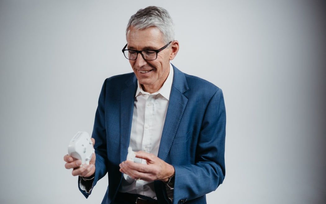Professor Ian Bissett wears a blue suit and holds a Insides co. device in his hands
