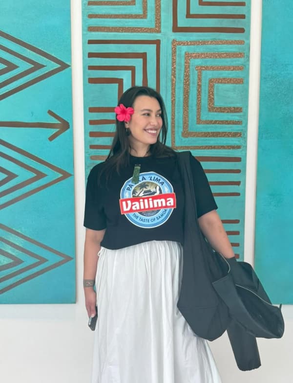 Isabella Moore - a smiling dark-haired woman with a red flower behind her ear - stands against a blue artwork.