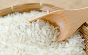 Raw white rice and wooden spoon in weave basket on sack background.