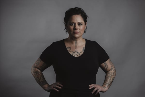 Image of Anika Moa looking at camera with hands on hips wearing a black t-shirt.