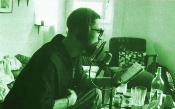 Hip hop producer Brainorchestra sitting in his lounge in front of a microphone and laptop recording.