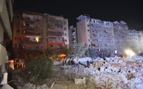 People watch as a blaze rages amid the smoldering rubble of a building destroyed in an Israeli air strike in the Haret Hreik neighborhood of Beirut's southern suburbs on September 27, 2024. A source close to Hezbollah says massive Israeli strikes on Beirut's southern suburbs flatten six buildings on September 27.