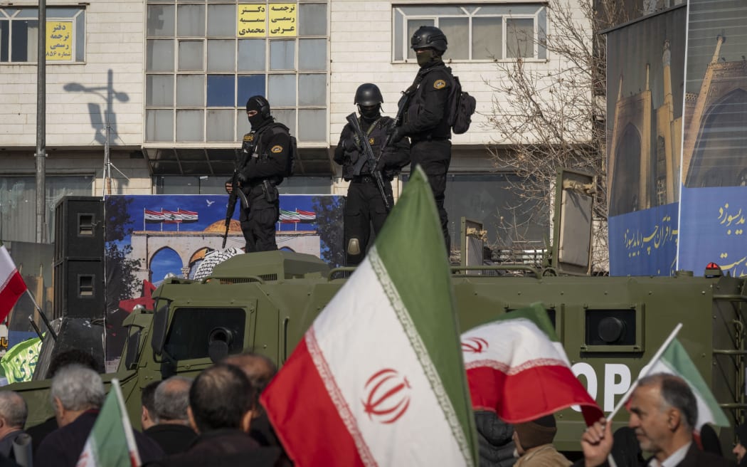 Armed members of Iran's police special forces monitor an area while standing on an armored military vehicle behind a country flag during a pro-Government rally in downtown Tehran, Iran, on January 12, 2026. The rally is held in Tehran against the recent anti-government unrest, opposition to the U.S. and Israel in Iran, and in support of Supreme Leader Ayatollah Ali Khamenei. (Photo by Morteza Nikoubazl/NurPhoto) (Photo by Morteza Nikoubazl / NurPhoto via AFP)