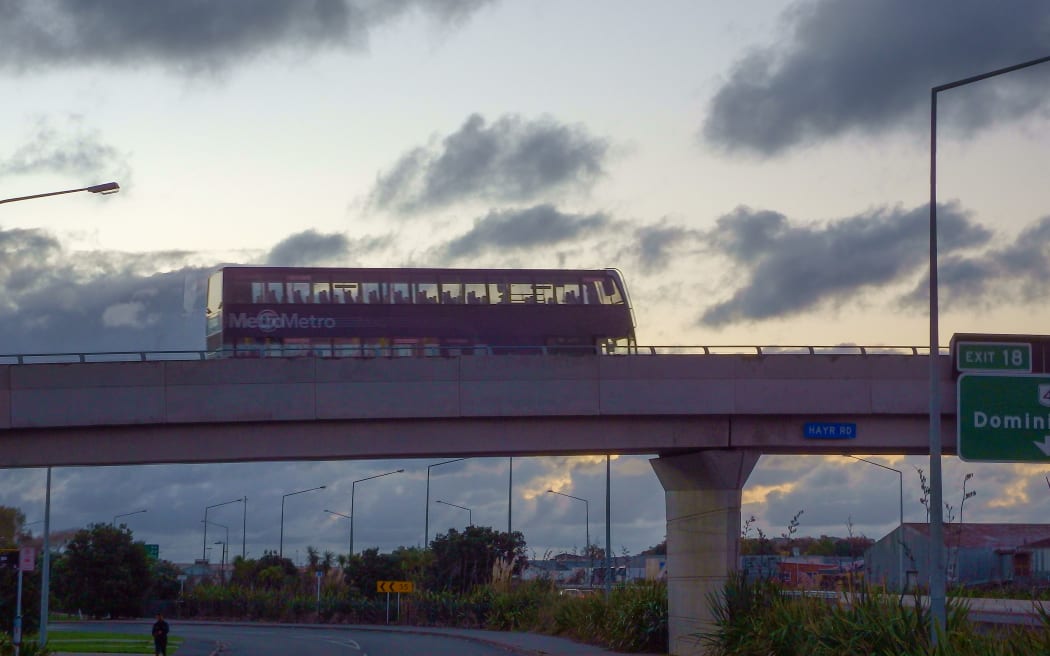 Double decker bus goes on a flyover against a back lit sky in Auckland New Zealand.