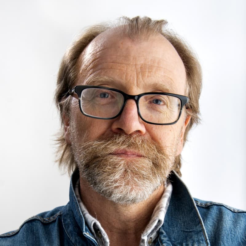 George Saunders wears a greying beard, dark-rimmed glasses and a denim acket.