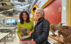 Isabel Castro (L) and Karen Mason standing side by side in a lab at Massey University. Isobel holds a stuffed kiwi.