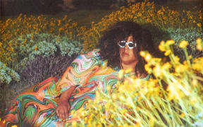 Cover image of Brittany Howard's album 'What Now'. Howard lies among flowers in a mountain scene.