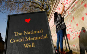 A woman draws red hearts representing individual coronavirus deaths onto the National Covid-19 Memorial Wall in London, England, on March 30, 2021.