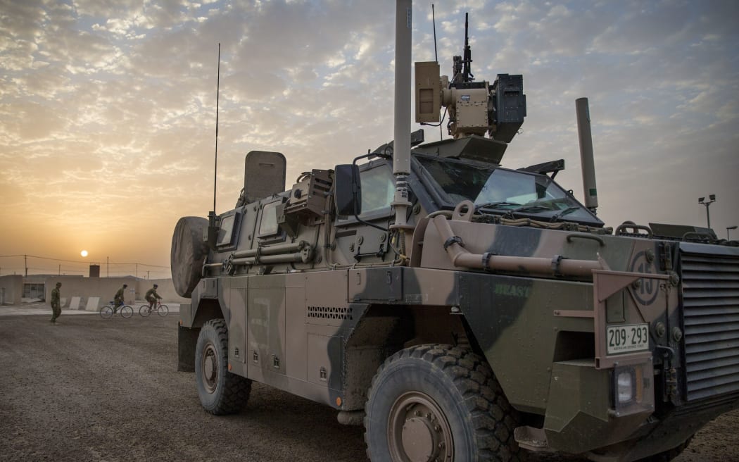 A camouflage painted armoured vehicle sits against a sunset