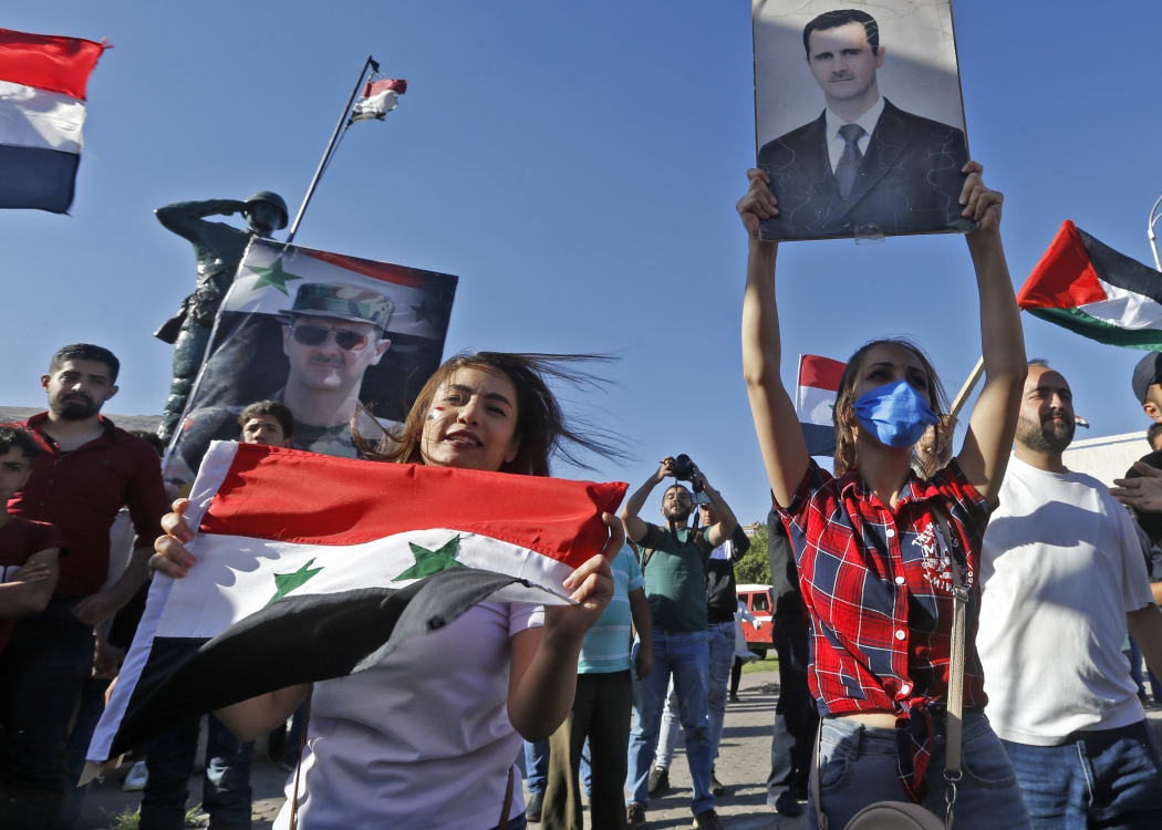 People wave Syrian national flags and pictures of President Bashar al-Assad during a demonstration in support of Assad and against US sanctions on the country, at the Umayyad Square in the centre of the capital Damascus on June 11, 2020.