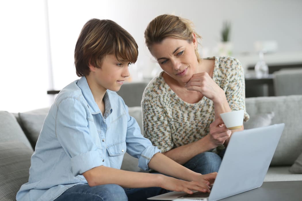 Mother looking after son doing homework on laptop