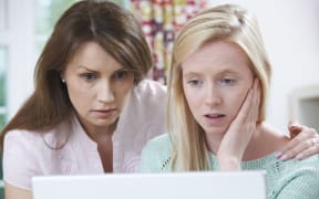 A photo of a concerned mother and daughter looking at a laptop