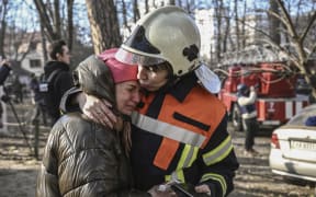 An evacuated resident is comforted by a rescue worker outside a burning apartment building in Kyiv on 15 March 2022, after strikes on residential areas.