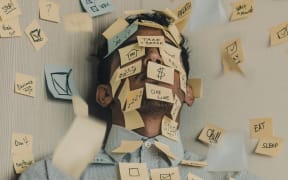 A man in a corner with post-it notes all over his face and the wall.