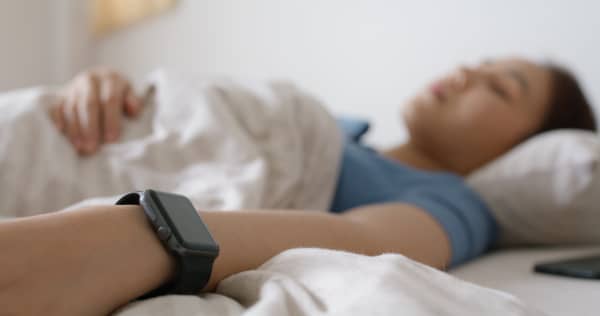 Young woman sleeping while wearing smartwatch for resting sleep rate on arm.