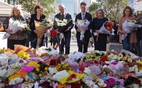 Australian Prime Minister Anthony Albanese (C) stands with New South Wales Premier Chris Minns (4th R) and other officials as they prepare to leave flowers outside the Westfield Bondi Junction shopping mall in Sydney on April 14, 2024, the day after a 40-year-old knifeman with mental illness roamed the packed shopping centre killing six people and seriously wounding a dozen others. (Photo by DAVID GRAY / AFP)